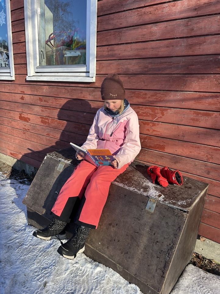 en person som sitter på en benk og leser en bok